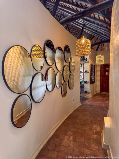 Many black-rimmed round mirrors arranged across a long pale wall, reflecting pendant lights and the lodge interior.