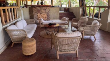 Wicker chairs and sofas around a small table beside a stone-faced hearth, with red tile floor and steps.