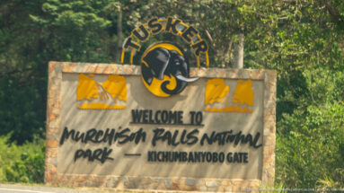 Stone sign reading “Welcome to Murchison Falls National Park — Kichumbanyobo Gate,” topped by a Tusker emblem.