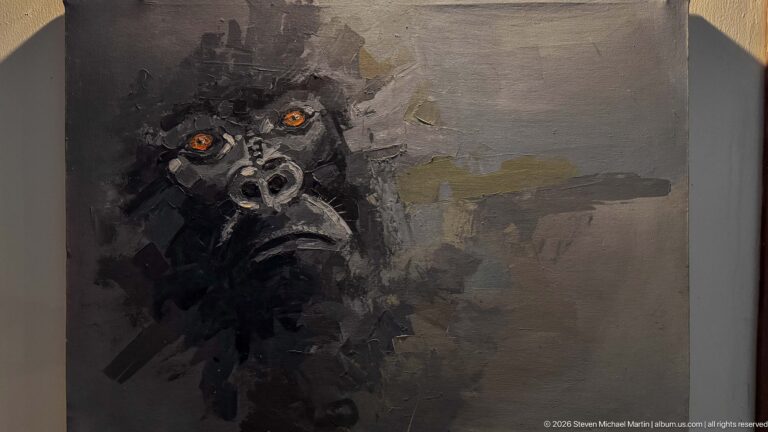Expressionistic gorilla portrait in black and gray paint with prominent orange-brown eyes.