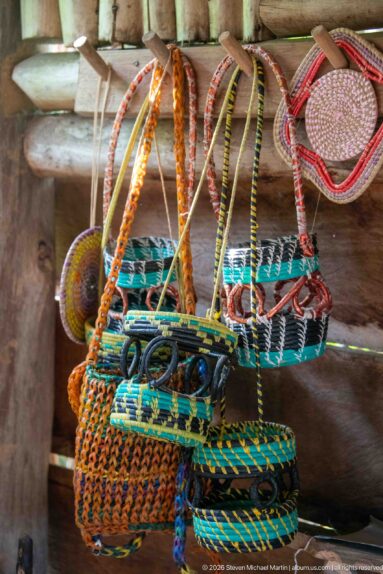 Colorful woven baskets, trays, and handled containers with spiral geometric patterns displayed against a wooden wall.