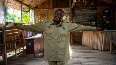 Smiling conservation staff member in khaki uniform stands with arms outstretched inside the bamboo rescue center visitor area.