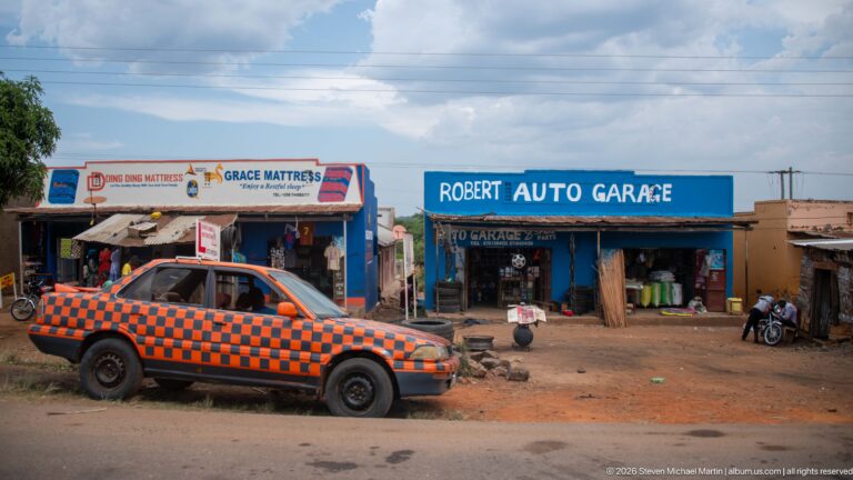 Robert Auto Garage and Grace Mattress storefronts with motorcycles, workshop goods, and an orange-and-black checker-painted car outside.
