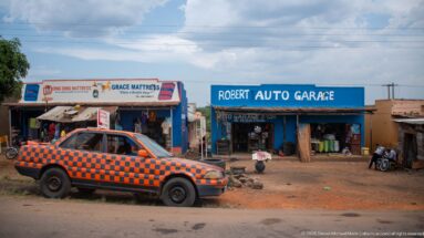 Robert Auto Garage and Grace Mattress storefronts with motorcycles, workshop goods, and an orange-and-black checker-painted car outside.