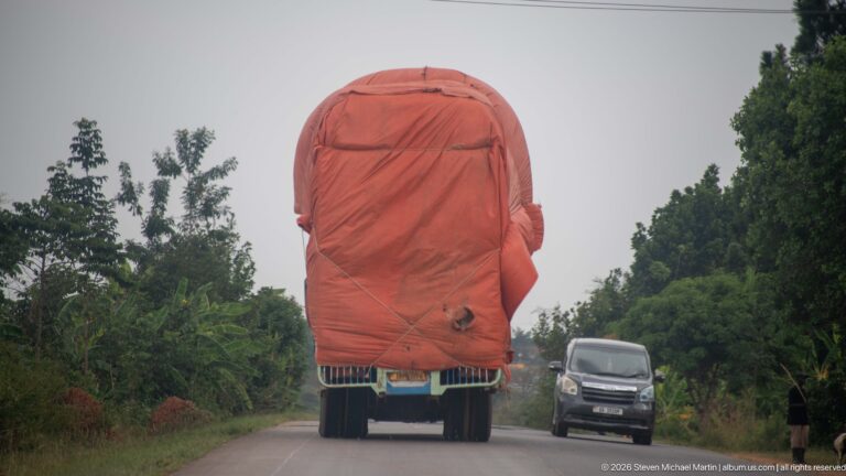Freight truck carrying a very tall reddish tarpaulin-covered load on a two-lane road with an oncoming van.