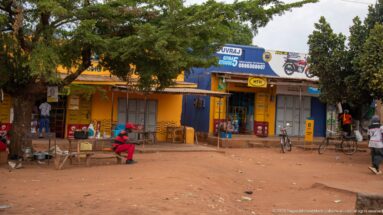 Yellow and blue roadside shops with MTN branding, large motorcycle signs, bicycles, stools, and people seated outside.