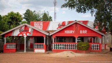 Red-and-white Hiburu Bar with Pilsner Lager branding, veranda, balustrade, and painted advertising across the façade.
