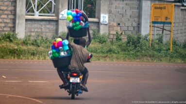 Rear view of motorcycle carrying tall stacks of colorful plastic bowls, cups, buckets, and basins in black containers.