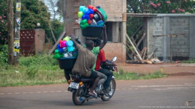 Motorcycle carrying brightly colored plastic basins, cups, buckets, and containers stacked high behind two riders.