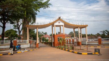 Arched entrance gate reading Kasana-Luweero Diocese, opening onto a landscaped drive and red-roofed buildings.