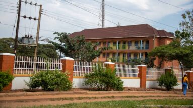 Two-story orange institutional building with balconies, hipped roof, white metal fence, and landscaped frontage.
