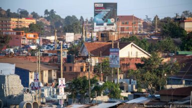 Elevated view of a busy Ugandan commercial district with traffic, billboards, low-rise shops, and larger brick buildings.