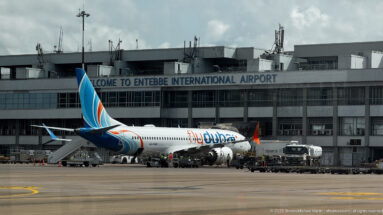 Flydubai jet parked beside the terminal at Entebbe International Airport with ground vehicles and service equipment on the apron.