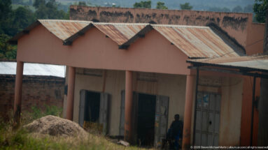 Pink masonry shop building with repeated peaked roof bays, corrugated roofing, and metal doors along a roadside.