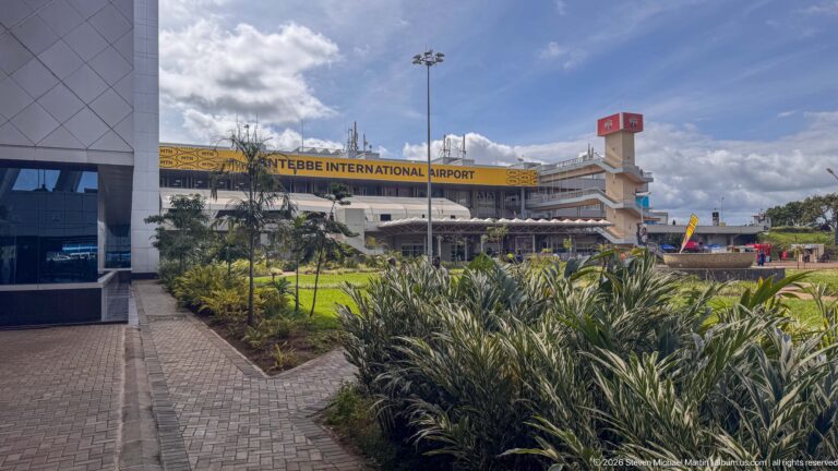 Landscaped walkway and ornamental planting leading toward the signed terminal of Entebbe International Airport.