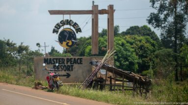Tusker-branded Master Peace Resort sign with directional arrow beside a motorcycle and rough timber shelter.