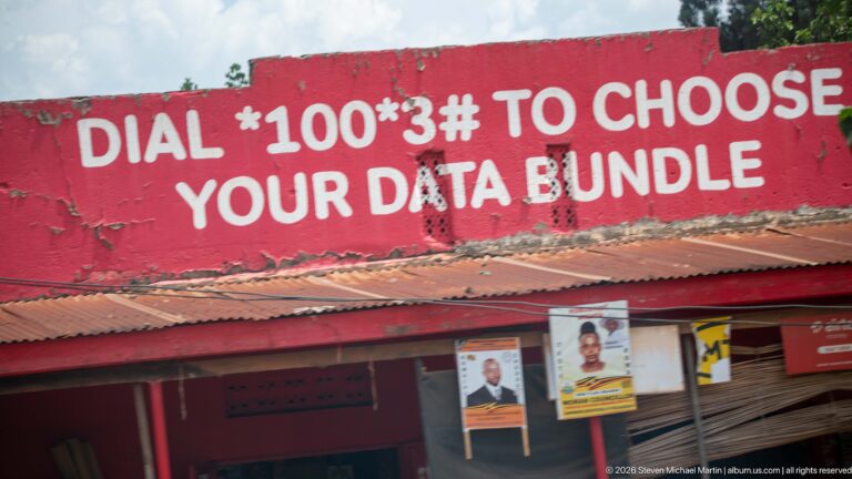 Red storefront painted with 'Dial *100*3# to choose your data bundle' above political posters and a corrugated awning.