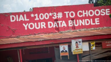 Red storefront painted with 'Dial *100*3# to choose your data bundle' above political posters and a corrugated awning.