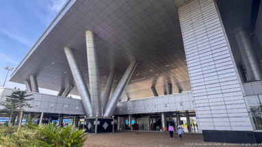Large airport canopy supported by angled silver columns above glass entrances and landscaped planting at Entebbe International Airport.