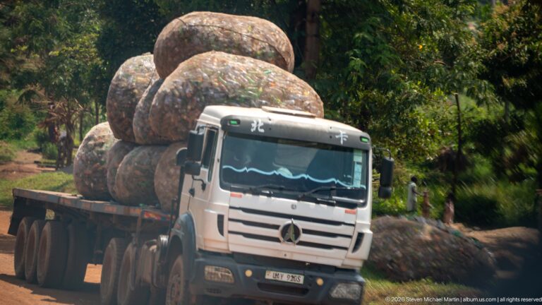 Mercedes flatbed truck carrying towering netted bales packed with used plastic bottles and containers.