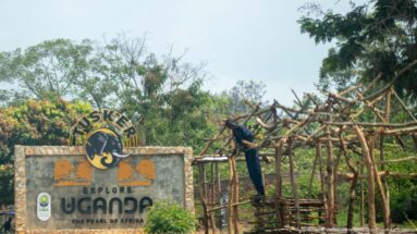 Tusker sign reading 'Explore Uganda — The Pearl of Africa' beside a man working on a rough timber framework.