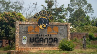 Tusker-branded masonry sign reading Explore Uganda, The Pearl of Africa, with a small UWA emblem.
