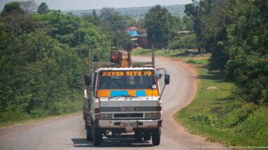 Isuzu cargo truck with orange-and-blue cab decoration and 'Never Give Up' lettering approaching on a rolling paved road.