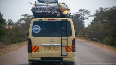Rear view of a beige Toyota van carrying mattresses, sacks, and bundled goods high on its roof rack.