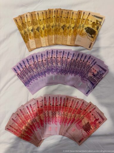 Three fanned rows of Ugandan shilling banknotes in yellow, purple, and red denominations arranged on a light surface.