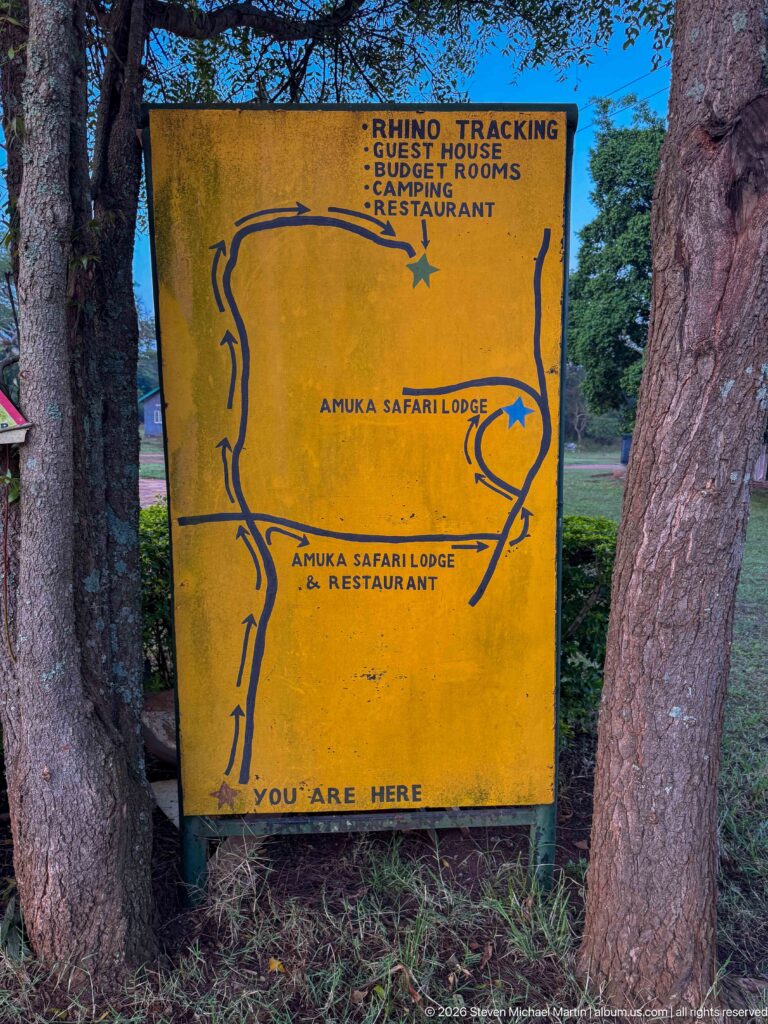 Yellow hand-painted map sign listing rhino tracking, guest rooms, camping, restaurant, reception, and Amuka Safari Lodge.