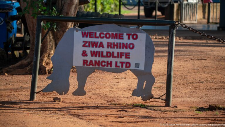 Entrance sign reading “WELCOME TO ZIWA RHINO & WILDLIFE RANCH LTD” above a rhinoceros silhouette on reddish ground.
