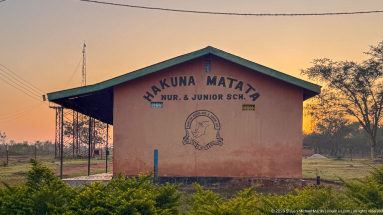 School building at sunset with painted words HAKUNA MATATA NUR. & JUNIOR SCH. and an emblem on the wall.