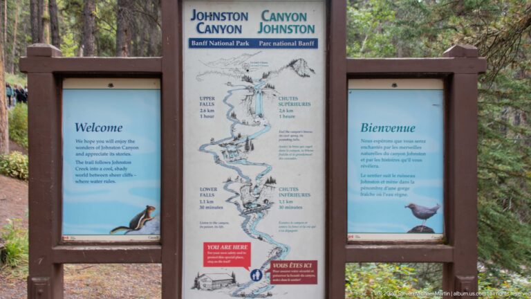 Johnston Canyon entrance sign with bilingual welcome panels and a map marking Upper and Lower Falls.