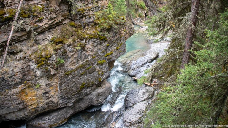 Creek drops over several rock ledges through a narrow ravine into a pale pool.