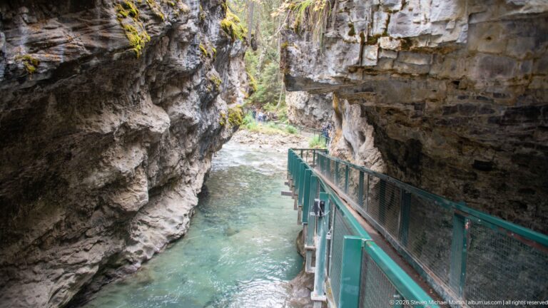 Green-railed boardwalk follows a clear creek between close, steep canyon walls in Banff National Park.