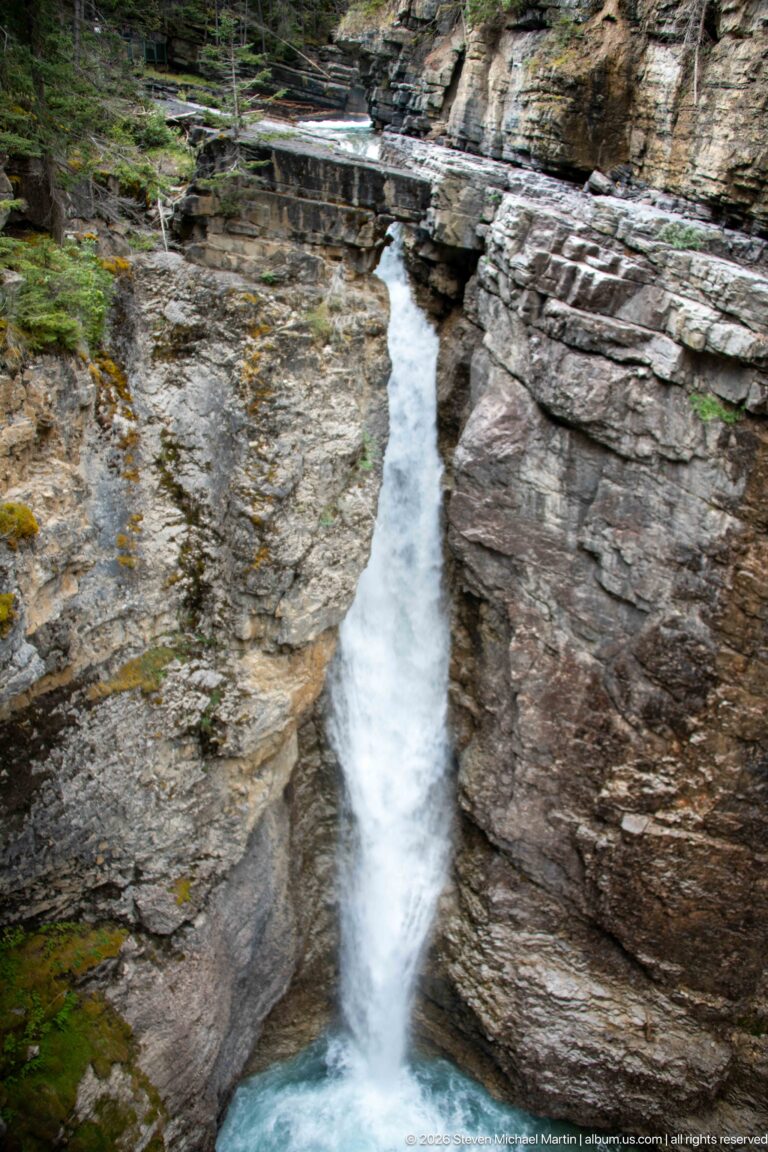 White cascade falling between horizontal rock shelves into a turquoise pool in Johnston Canyon.