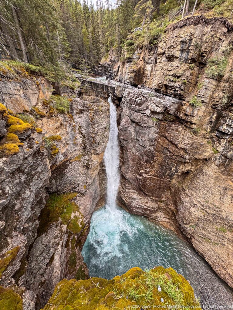 Waterfall and turquoise pool framed by broad, stratified canyon walls and mossy ledges.
