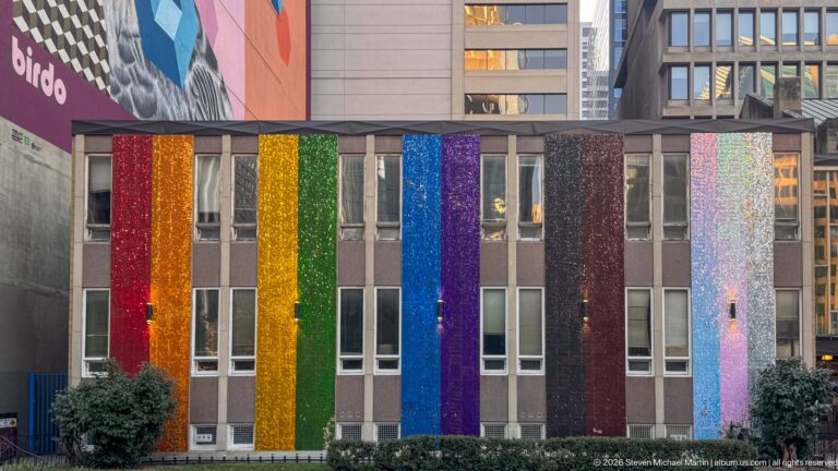 Downtown Calgary building façade covered in vertical rainbow-colored and shimmering panels between rows of windows.