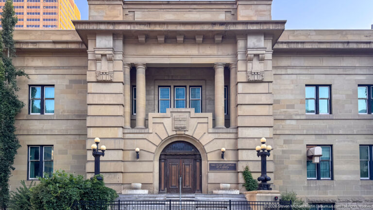 Calgary Courthouse No. 2 sandstone entrance with recessed arch, paired columns, broad steps, globe lamps, and symmetrical windows.