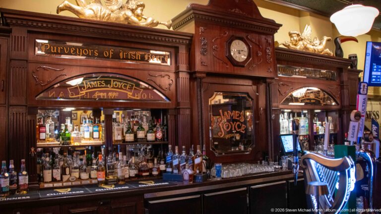 Ornate carved-wood James Joyce pub bar with bottles, mirrors, clock, and Purveyors of Irish Beer lettering.