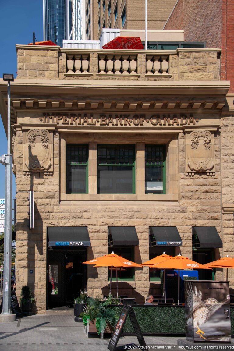 Historic Imperial Bank of Canada stone façade with carved lettering and restaurant patio umbrellas below.