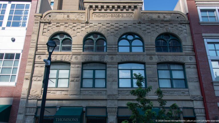 Stone façade of the Thomson Bros. Block with carved name panel, rounded upper windows, and modern storefront.
