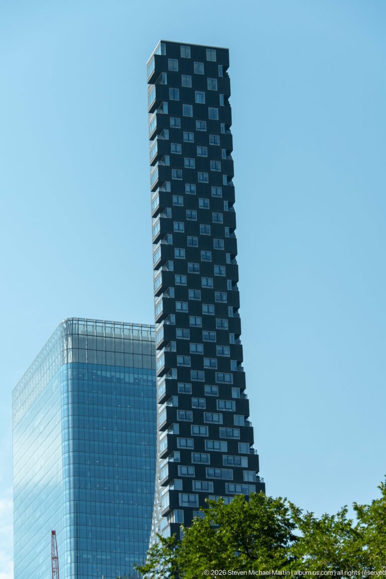 Dark residential high-rise with staggered balconies in front of a broad glass office tower in Calgary.