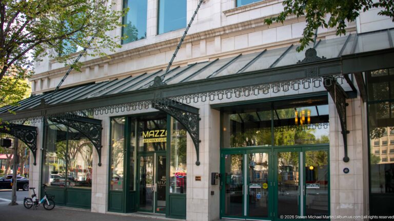 Green restaurant storefront beneath an ornate glass-and-metal canopy on a pale stone Calgary building.