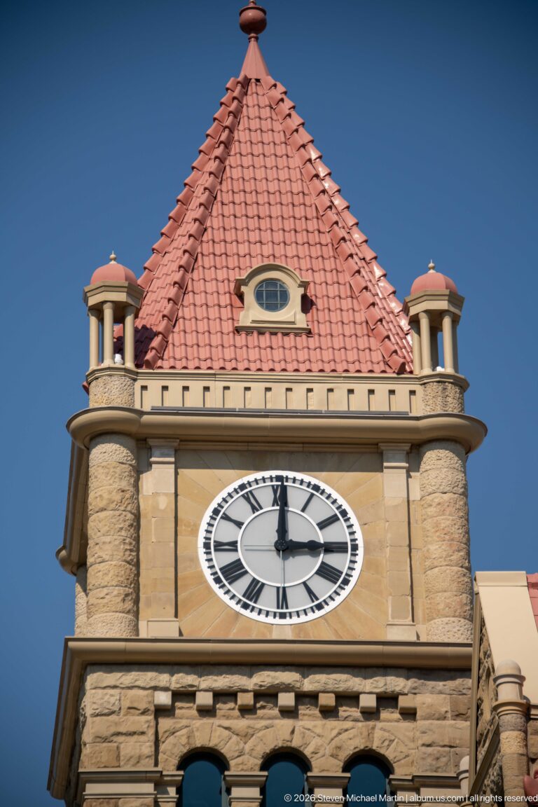 Clock face, sandstone tower, corner turrets, and red-tiled roof of historic Calgary City Hall.