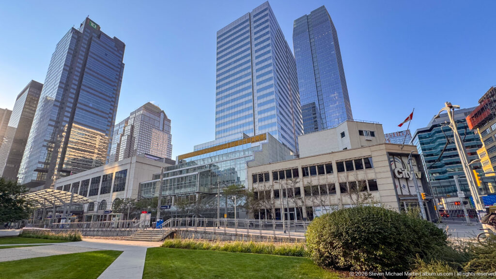 Calgary civic complex and lawn with the Municipal Building in front of tall glass-and-steel downtown office towers.
