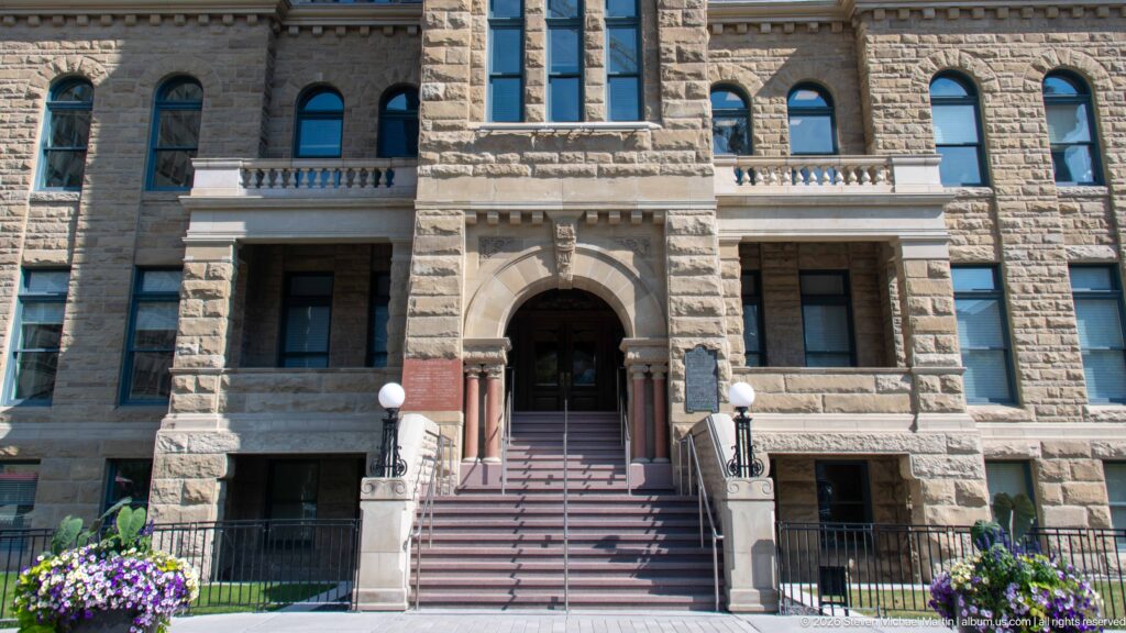 Central arched entrance and broad staircase on the rough sandstone façade of historic Calgary City Hall.