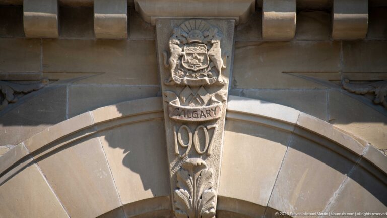 Carved Calgary coat of arms and 1907 date stone centered above a sandstone arch at historic City Hall.