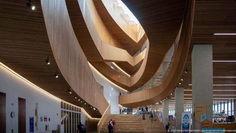 Curving wood-clad balconies sweeping above a broad staircase in Calgary Central Library’s tall atrium.