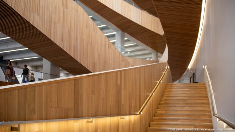 Wood staircase with illuminated handrails beneath sweeping timber balconies inside Calgary Central Library.